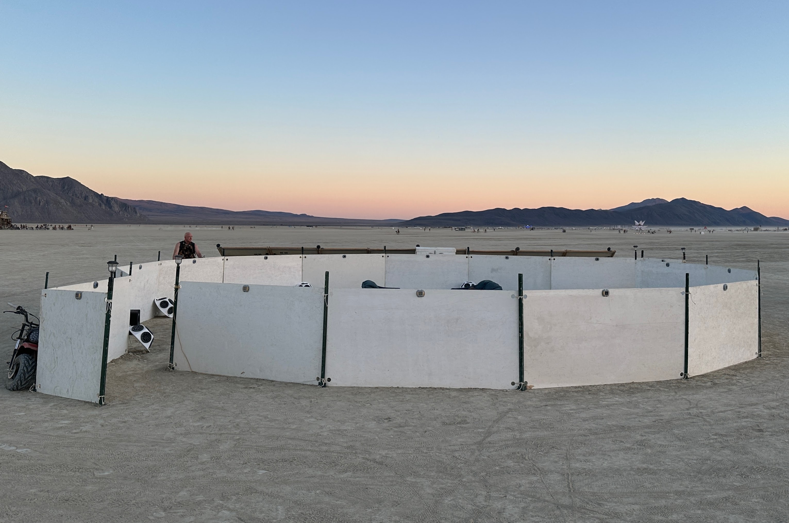 a circle of low white walls surrounds a sound installation in the desert in bright daylight