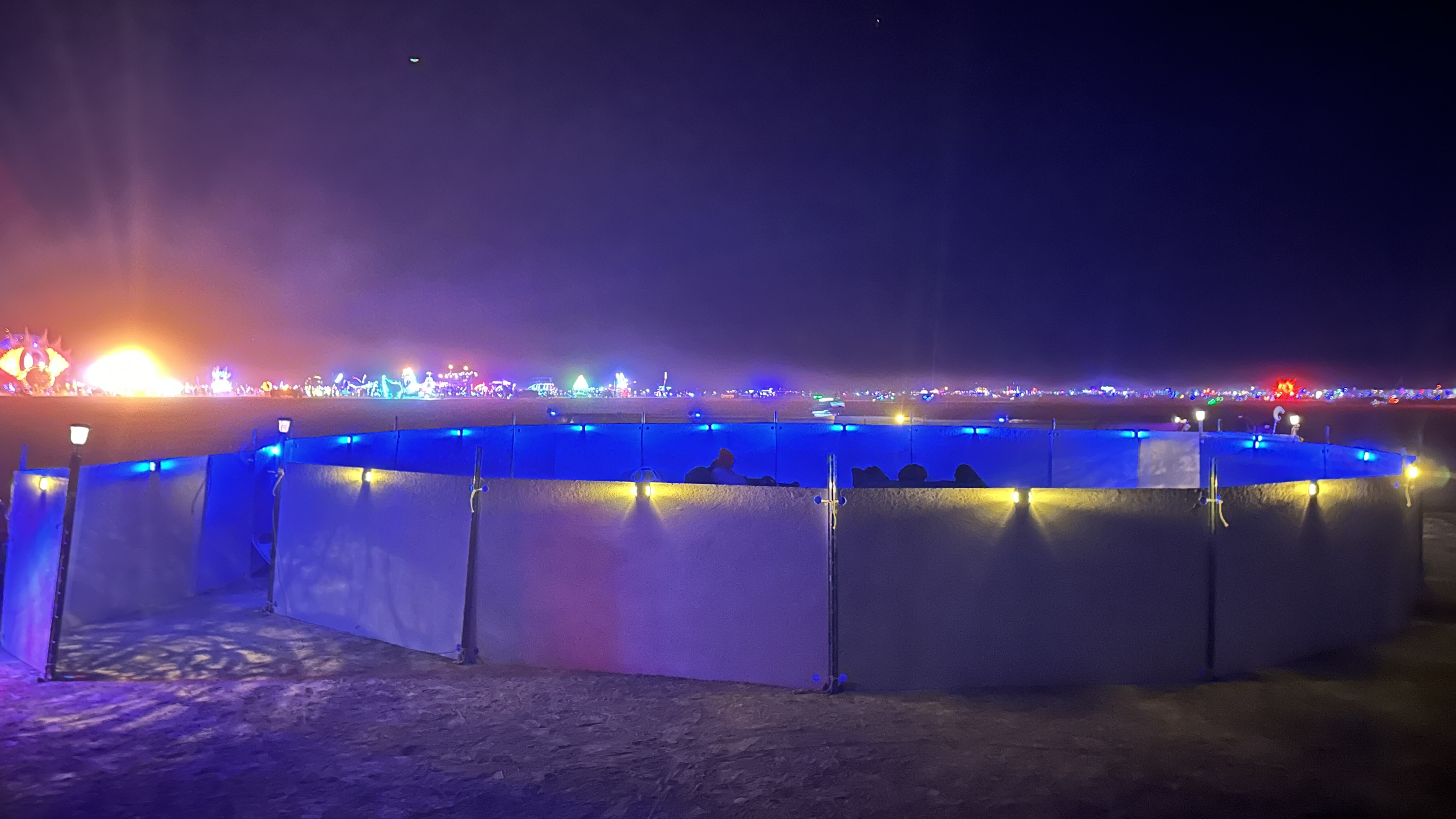 a circle of low white walls surrounds a sound installation in the desert, lit up with blue and white LED lights at night